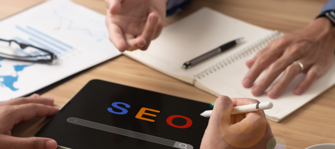 Digital marketers in a meeting analyzing SEO strategies with a tablet displaying 'SEO' and charts on the table.
