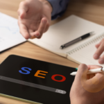Digital marketers in a meeting analyzing SEO strategies with a tablet displaying 'SEO' and charts on the table.