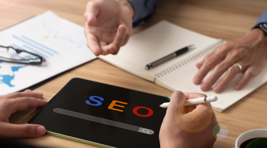 Digital marketers in a meeting analyzing SEO strategies with a tablet displaying 'SEO' and charts on the table.
